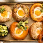 Overhead photo of five bagel eggs on a parchment lined tray with a bowl of avocado salsa.