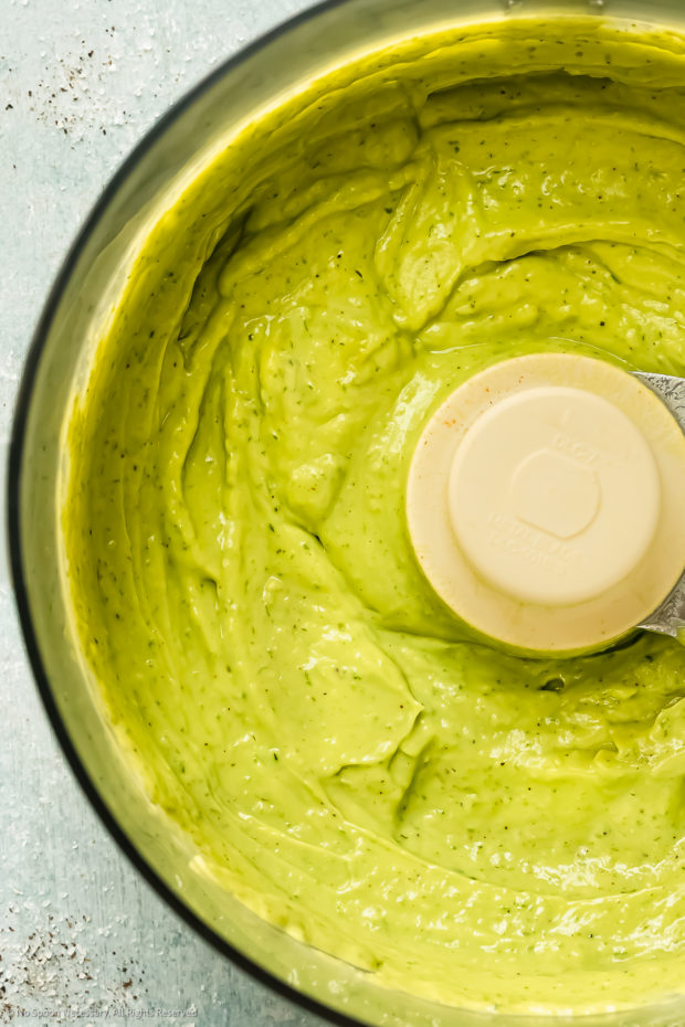 Overhead close-up photo of creamy green goddess in the bowl of a food processor.