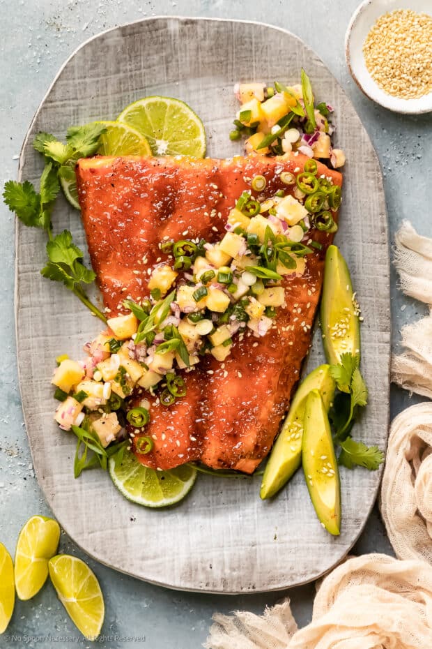Overhead photo of a hot honey salmon filet topped with pineapple salsa and diced avocado on a serving platter.