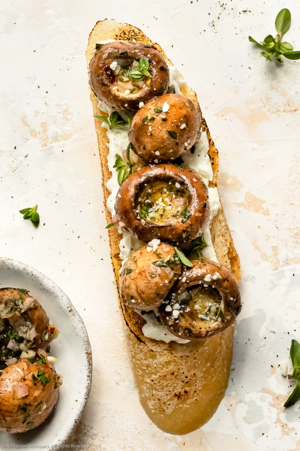 Overhead photo of marinated mushrooms on a piece of toasted baguette with goat cheese - photo of how to use marinated mushrooms.
