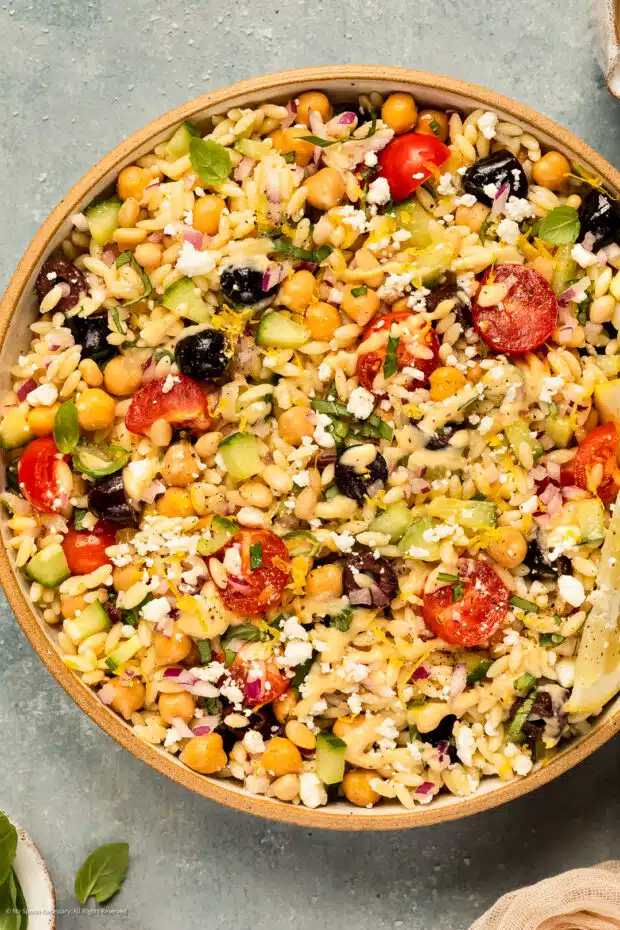 Overhead photo of orzo pasta salad with tomatoes, cucumbers, and feta in a white bowl.