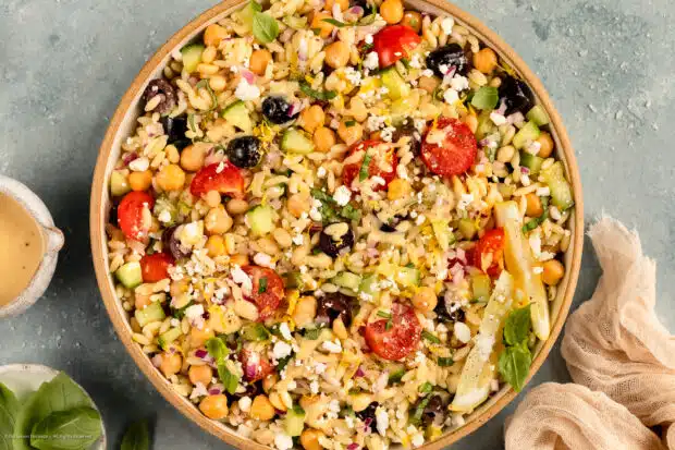 Overhead photo of orzo pasta salad with tomatoes, cucumbers, olives and feta in a serving bowl.