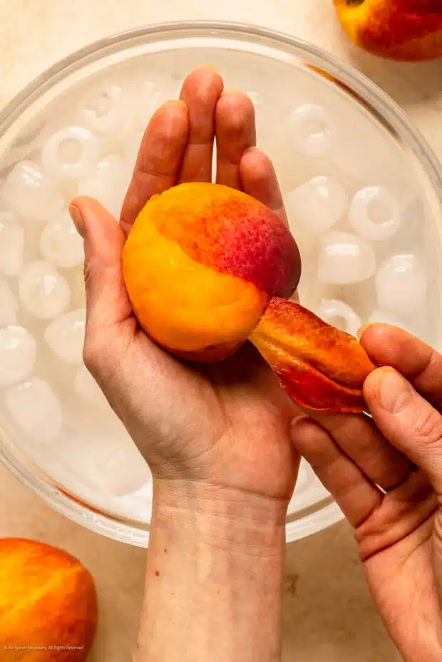 Action photo of a person peeling the skin from a peach.