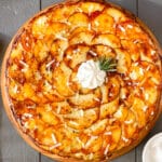 Photo of layered potato galette with cheese and rosemary on a wood board.