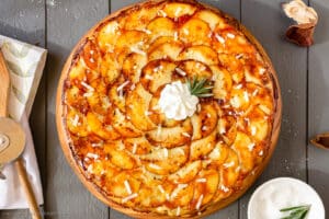 Photo of layered potato galette with cheese and rosemary on a wood board.