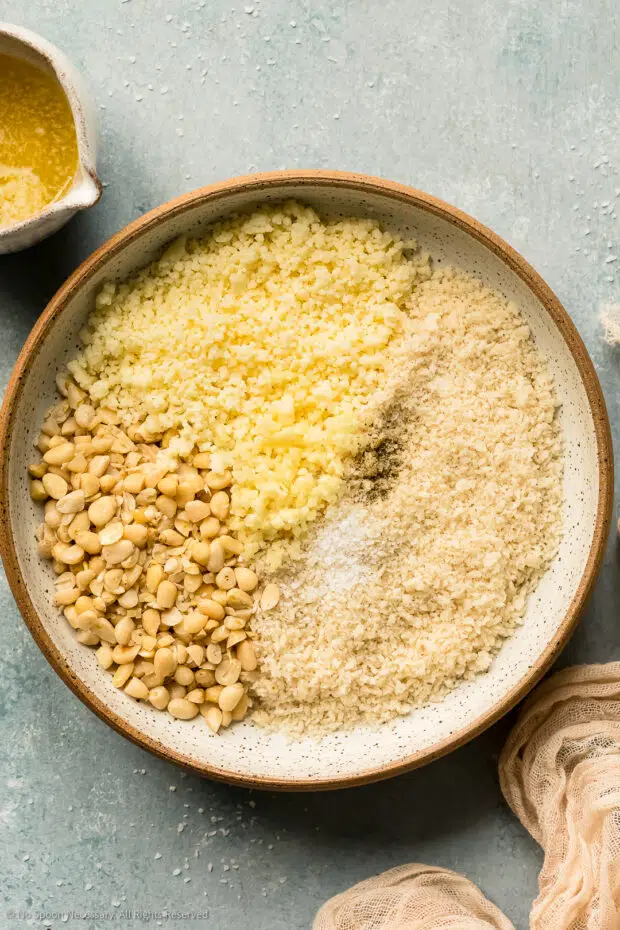 Overhead photo of the ingredients for au gratin topping - cheese, pine nuts and panko - in a mixing bowl.