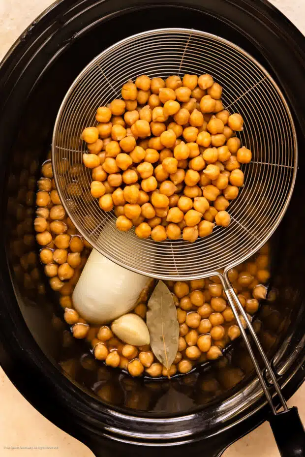 Overhead photo of slow cooker chickpeas draining on a stainless steel kitchen strainer.