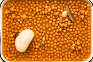 Overhead photo of a kitchen tray with perfectly homed cooked dried chickpeas in their cooking liquid.