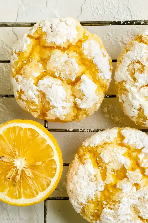 Close-up photo of two lemon crinkle cake mix cookies with a lemon wedge next to the cookies.