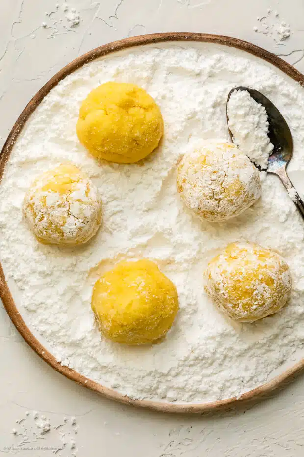 Overhead photo of five lemon cookie dough balls sitting in a bowl of powdered sugar.