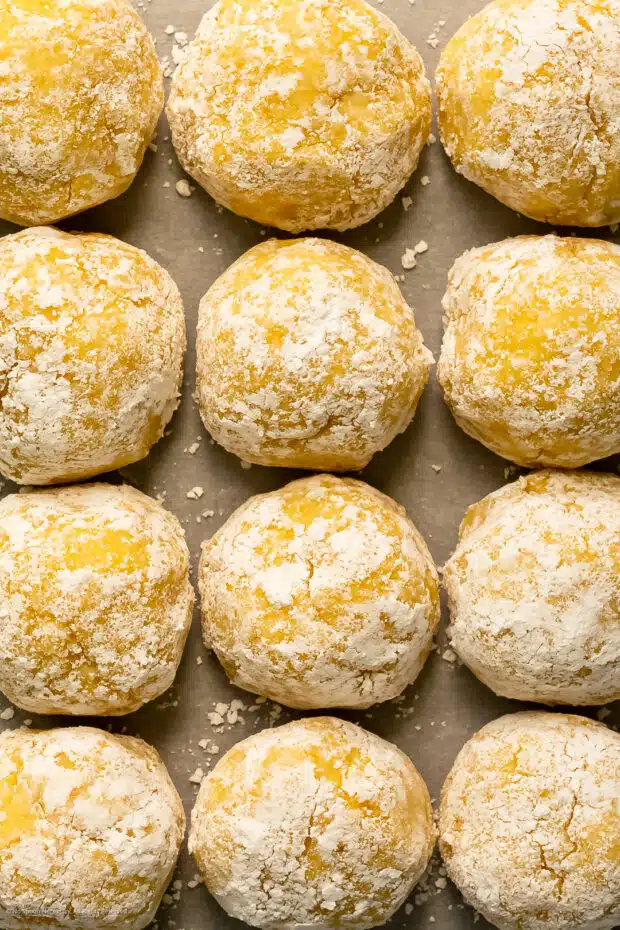 Close-up photo of a dozen lemon crinkle cookie dough balls rolled in powdered sugar.