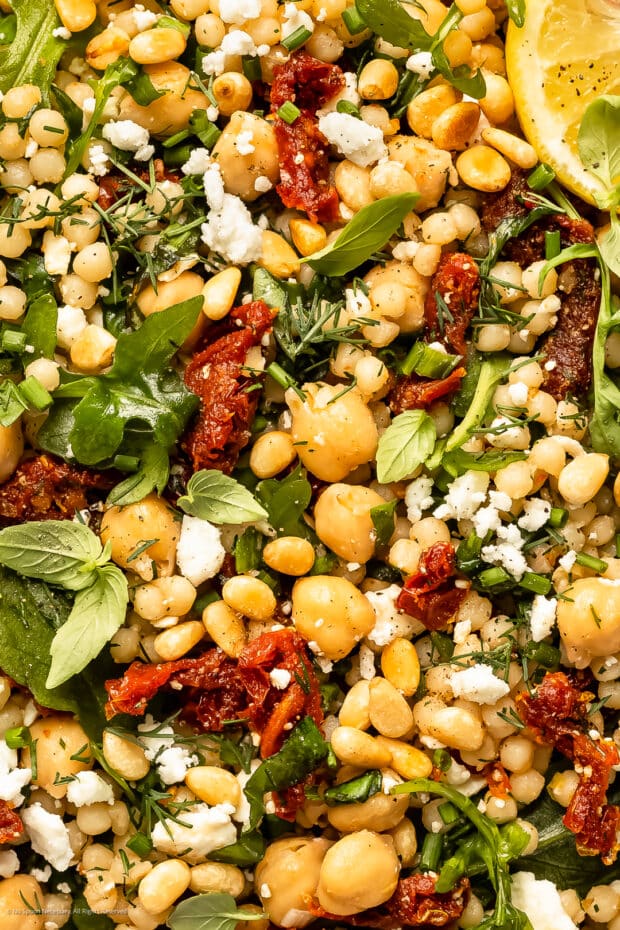 Close-up photo of cooked pearl couscous with sun-dried tomatoes, chickpeas, arugula, and feta.