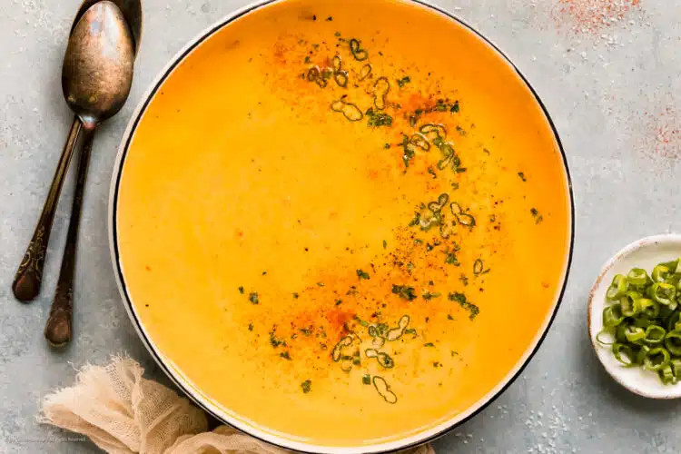 Overhead photo of beer cheese soup garnished with paprika and fresh herbs in a white pot.