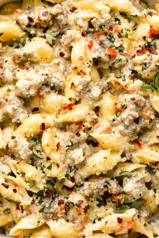 Overhead, extreme close-up photo of Italian sausage pasta garnished with crushed red pepper flakes, fresh parsley and chopped thyme. 