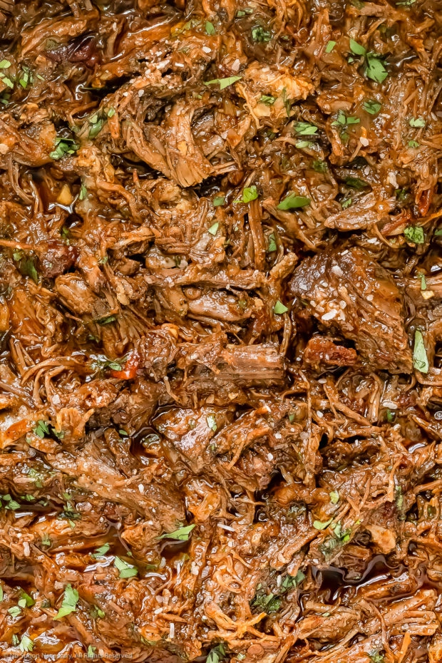 Overhead, extreme close-up photo of tender pulled beef barbacoa garnished with chopped fresh cilantro.