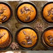 Overhead landscape photo of pumpkin chocolate chip muffins in a muffin pan with roughly chopped dark chocolate and cinnamon sugar strewn on top of the pan.