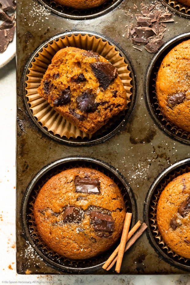 Overhead close-up photo of a halved pumpkin muffin in a muffin pan showcasing the inside texture of the muffin and the large melted chocolate chunks. 