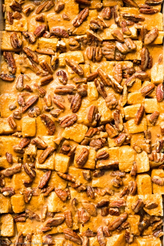 Overhead close-up photo of bread cubes and pecans covered and soaked in a pumpkin egg custard.