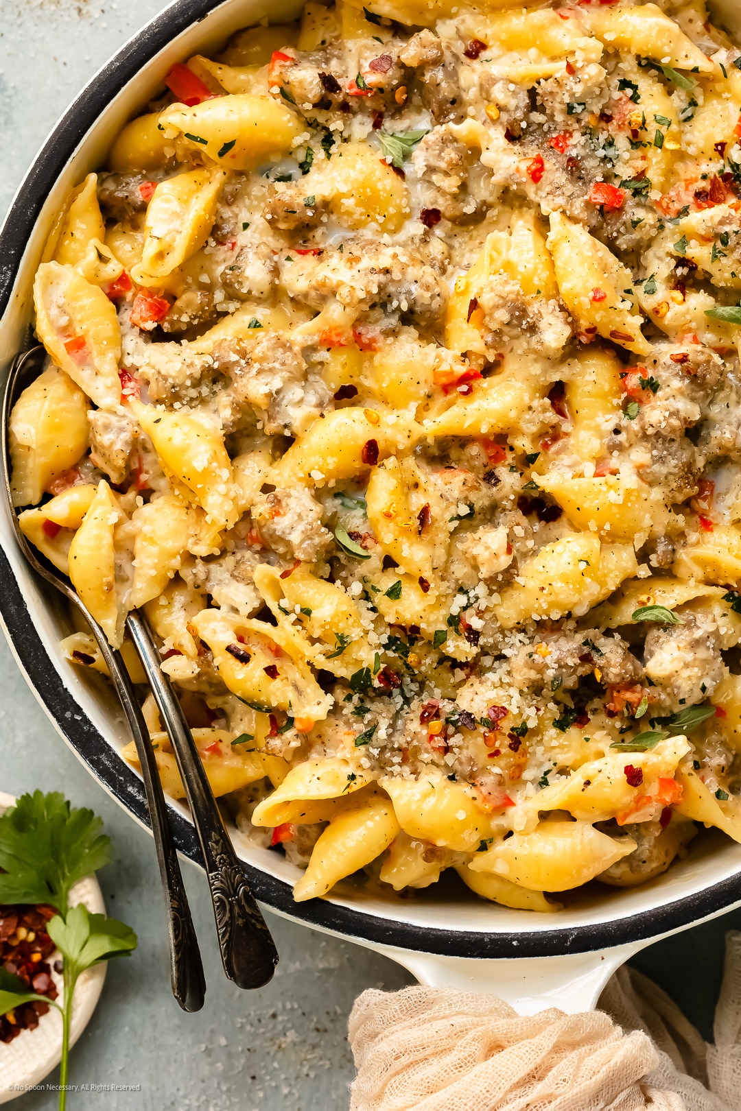 Overhead photo of sausage and cream pasta with bell peppers and cheese in a white skillet.