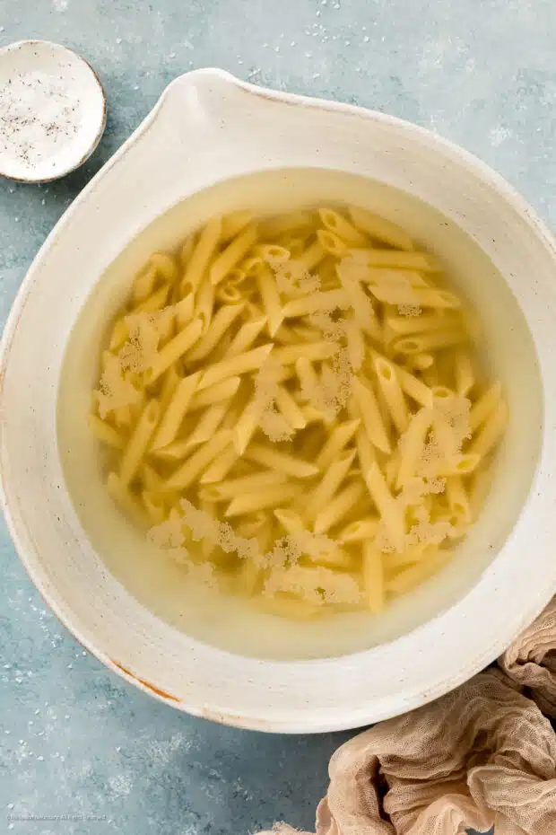Overhead photo of ziti pasta soaking in a bowl of hot water.