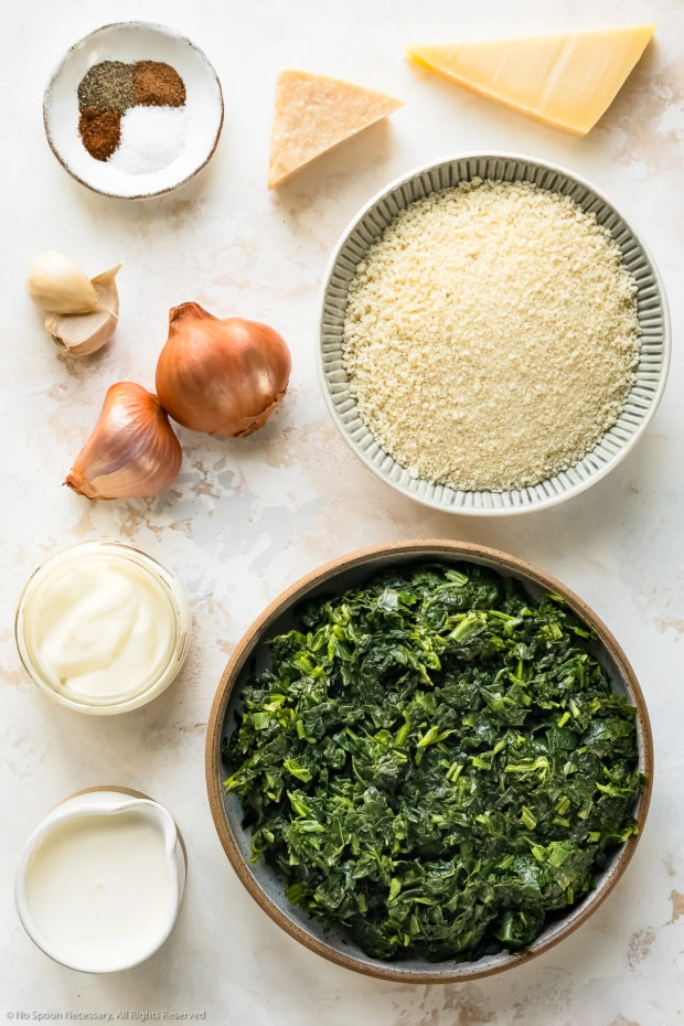 Overhead photo of all the ingredients in creamed spinach casserole neatly organized on a white surface.