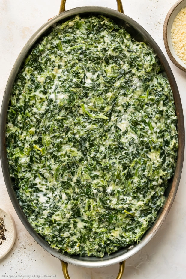 Overhead photo of creamed spinach in an oval baking dish before being topped with breadcrumbs.