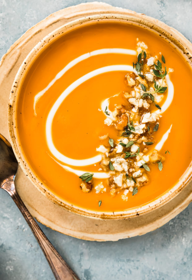 Overhead photo of Creamy Sweet Potato Soup topped with fresh thyme and walnuts in a beige soup bowl.