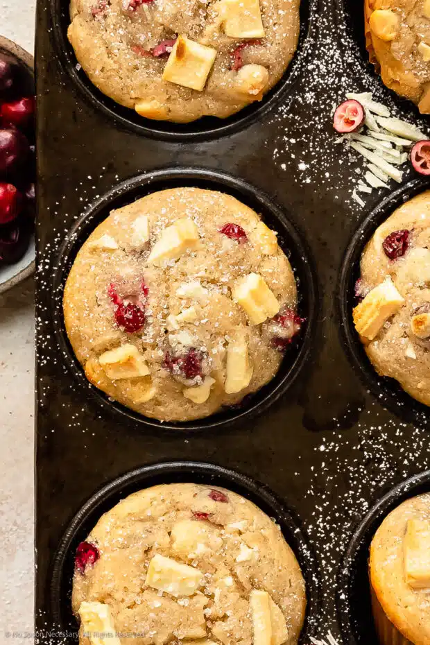 Overhead, close-up photo of a freshly baked white chocolate cranberry muffin in a muffin tin.