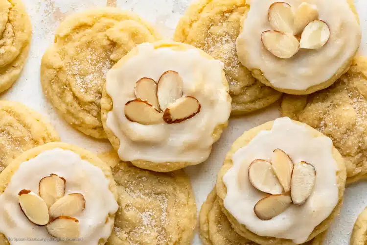 Overhead photo of a dozen soft almond sugar cookies spread out on a white surface.