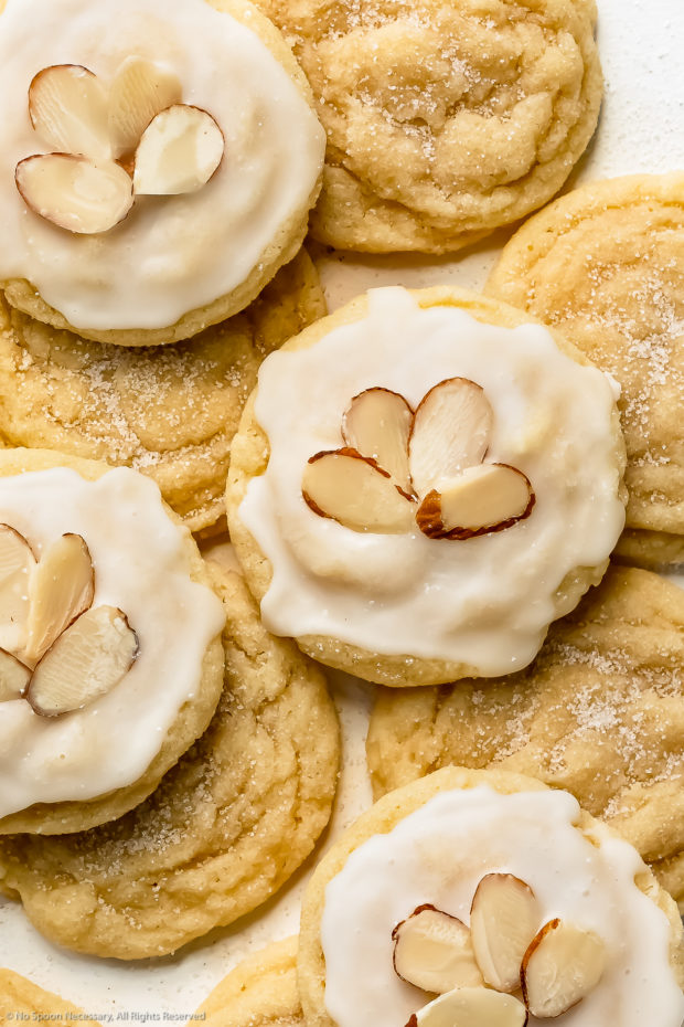 Overhead close-up photo of a iced almond sugar cookie resting on a stack of cookies.