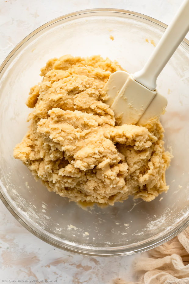 Overhead photo of a raw easy sugar cookie dough in a glass mixing bowl with a spatula inserted into the dough.