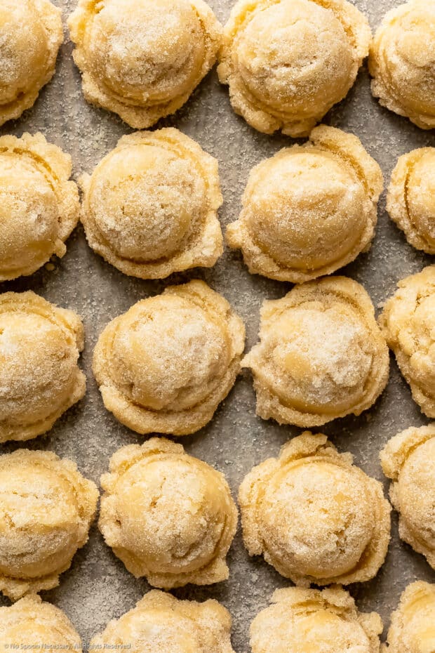 Close-up photo of individual raw sugar cookie almond dough balls arranged on a baking sheet.