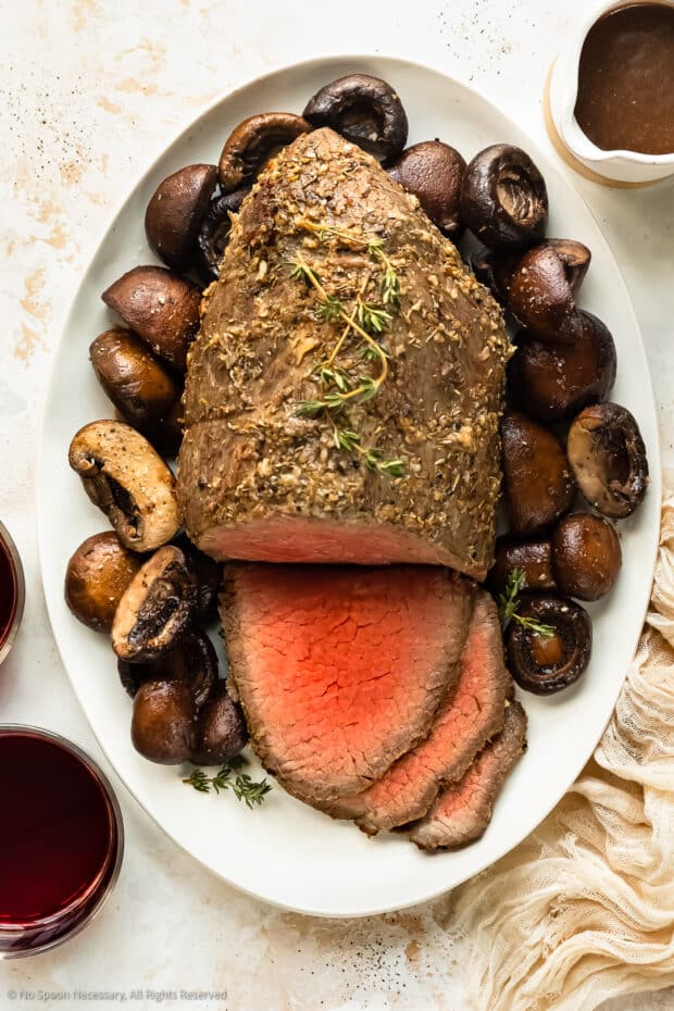 Overhead photo of a partially sliced eye of round roast with mushrooms on a serving platter. 