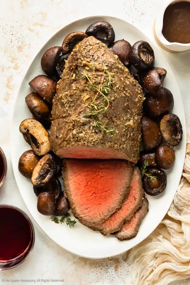 Overhead photo of a partially sliced eye of round roast with mushrooms on a serving platter. 