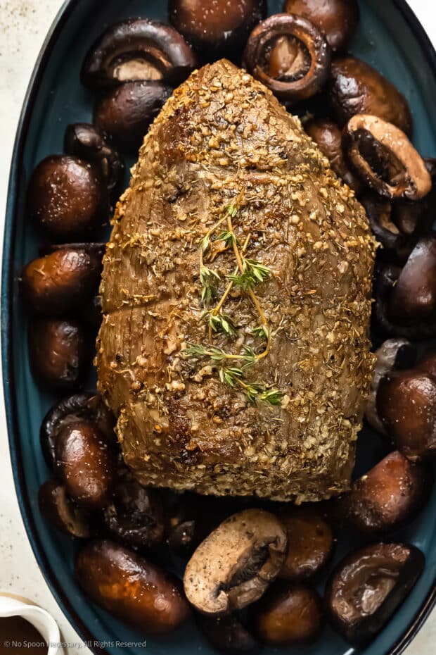 Photo of a eye of round beef roast with mushrooms in a large roasting pan.