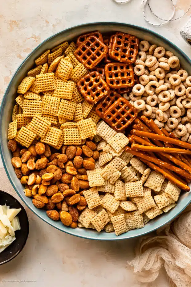 Overhead photo of all the snack ingredients for making chex mix sweet recipe neatly arranged in a large mixing bowl. 