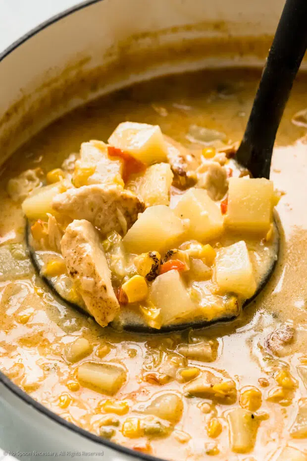 Straight on photo of a ladle scooping corn chowder with chicken from a pot.