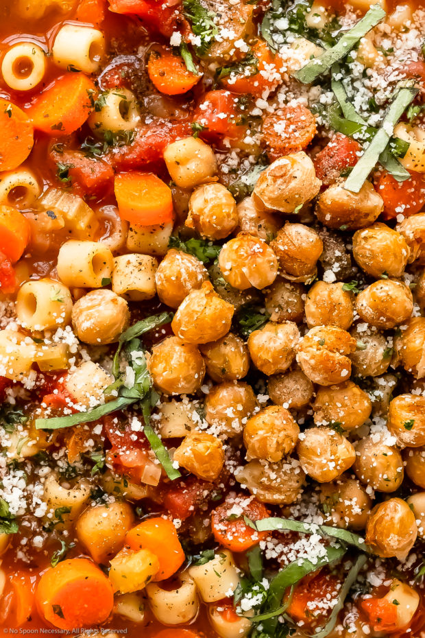 Overhead close-up photo of vegetable soup garnished with crispy chickpeas, grated parmesan and fresh basil.