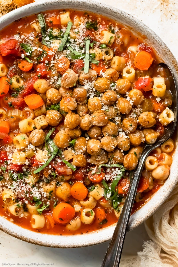Overhead photo of Italian Pasta e Ceci garnished with crispy chickpeas in a white bowl with a serving spoon tucked into the side of the soup.