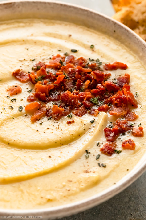 Angled, close-up photo of creamy winter vegetable soup topped with crispy bacon.