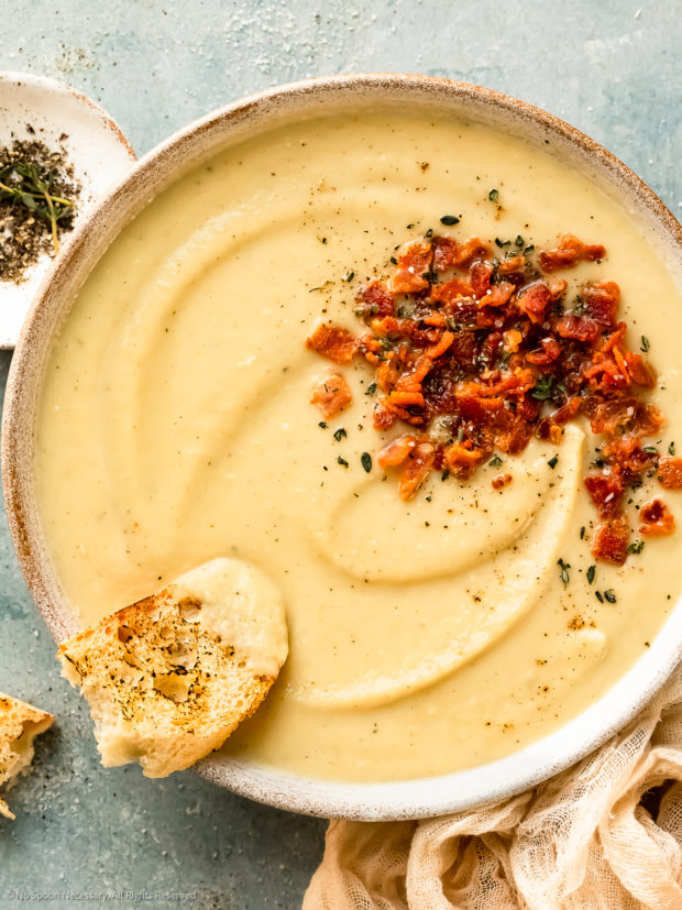 Overhead photo of a bowl of creamy parsnip soup with a torn piece of baguette dipped into the soup.