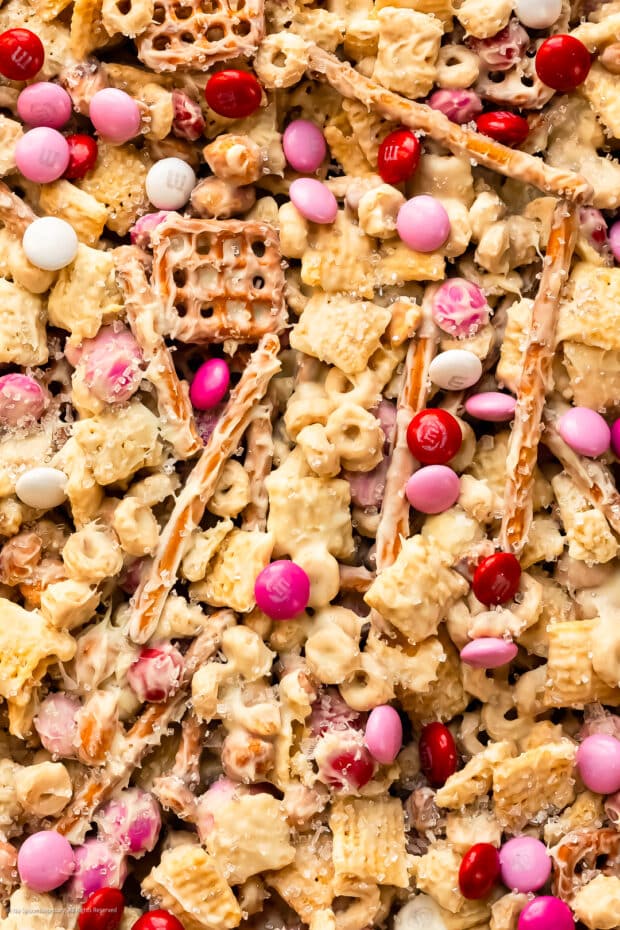 Up-close overhead photo of a sweet snack mix with white chocolate, cereals, nuts, and pretzels.