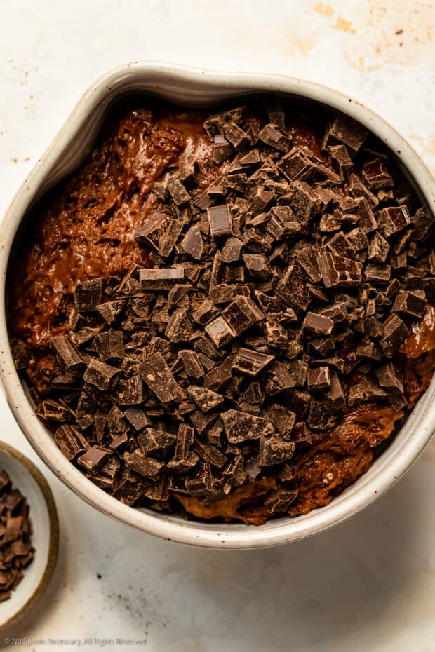 Overhead photo of a chocolate muffin batter topped with chocolate chunks in a large mixing bowl.