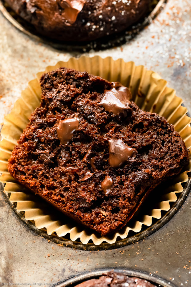 Angled, close-up photo of a bakery style chocolatey muffin broken in half to showcase the fudgy, melty chocolate center.