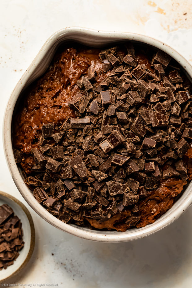 Overhead photo of a large mixing bowl filled with chocolate muffin batter topped with coarsely chopped chocolate - photo of step 6 of the recipe.