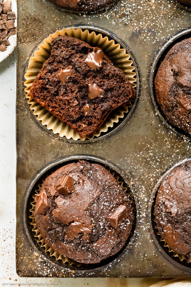 Overhead photo of a muffin tin holding a double chocolate muffin broken in half to expose the melty, fudgy chocolate center.