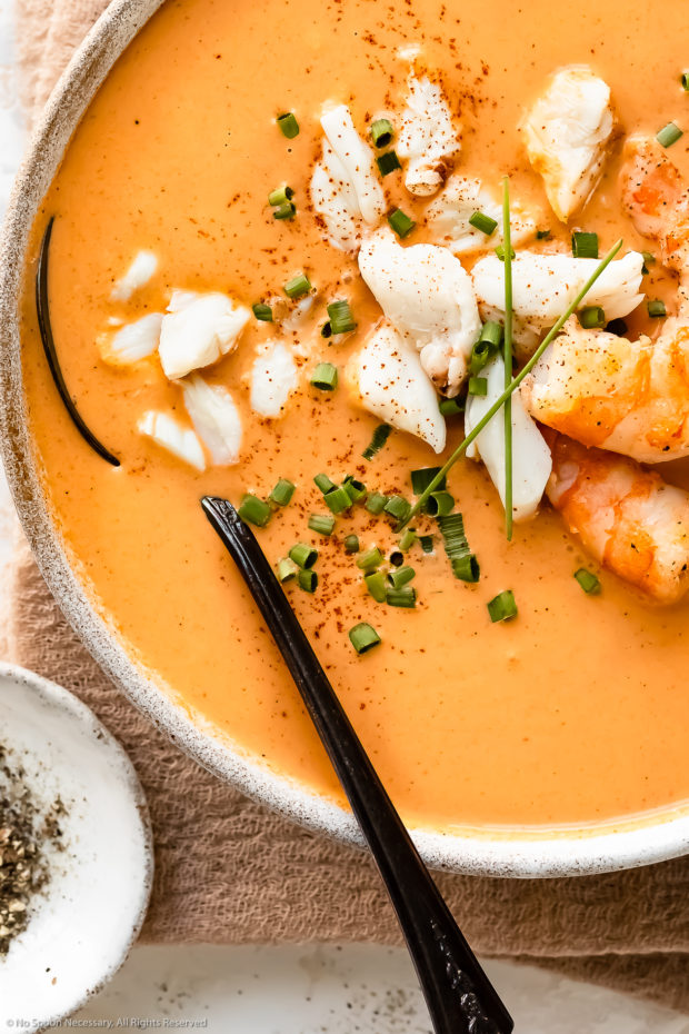 Overhead, close-up photo of Crab and Shrimp Bisque garnished with snipped chives in a white soup bowl with a spoon inserted into the bisque lifting up large chunks of lump crab.
