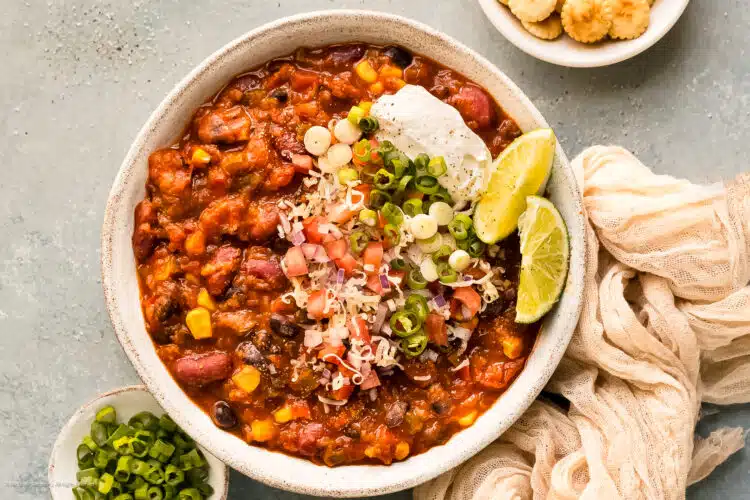 Overhead photo of a bowl of 3 bean chili garnished with diced tomatoes, sliced green onions, and a dollop of sour cream.