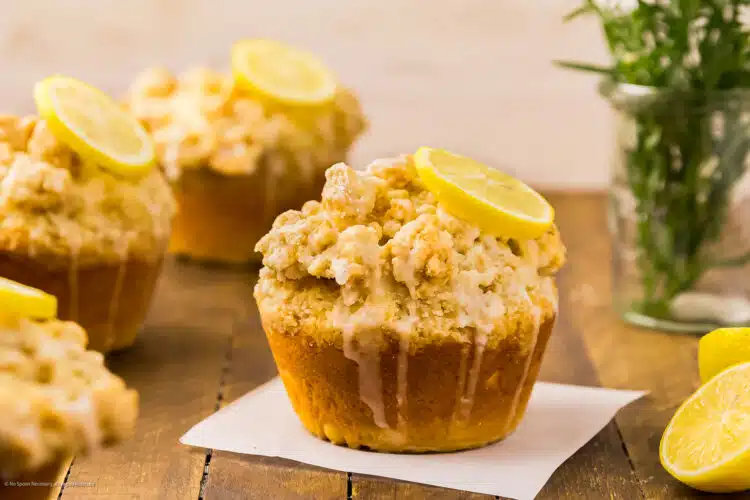 Straight on photo of a four perfect lemon muffins with crumb topping and lemon glaze.