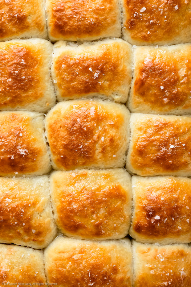 Overhead, close-up photo of soft bread rolls brushed with melted butter and sprinkled with sea salt.